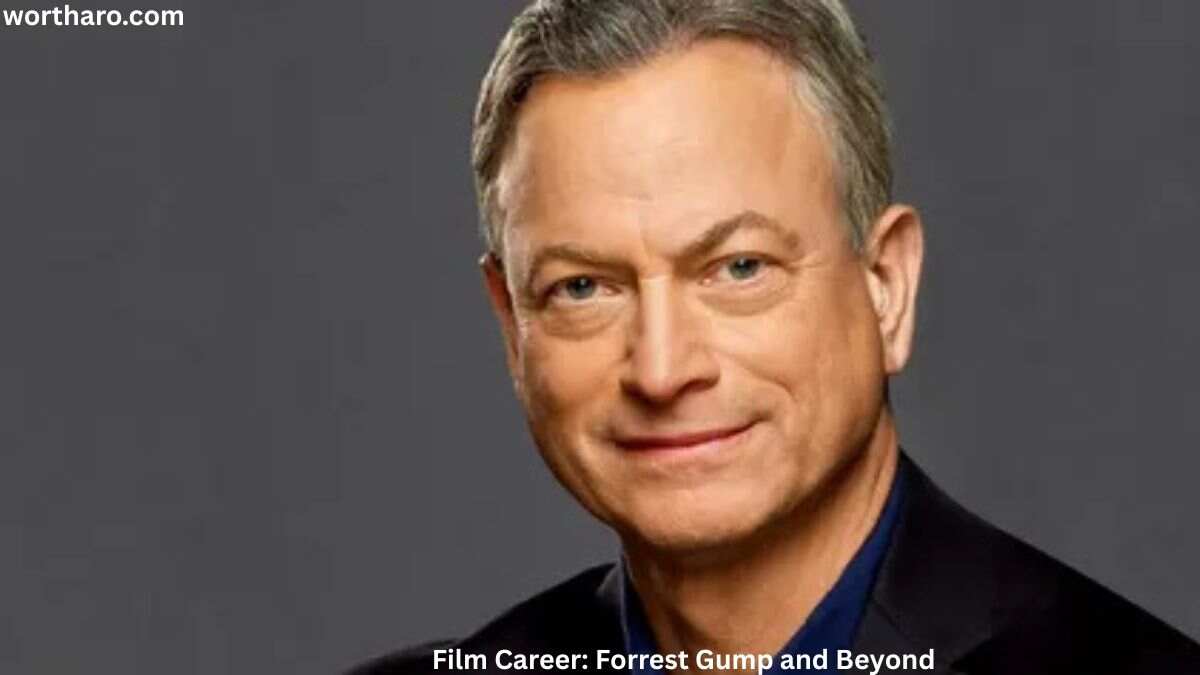 Gary Sinise close-up portrait in a dark suit, smiling against a grey background
